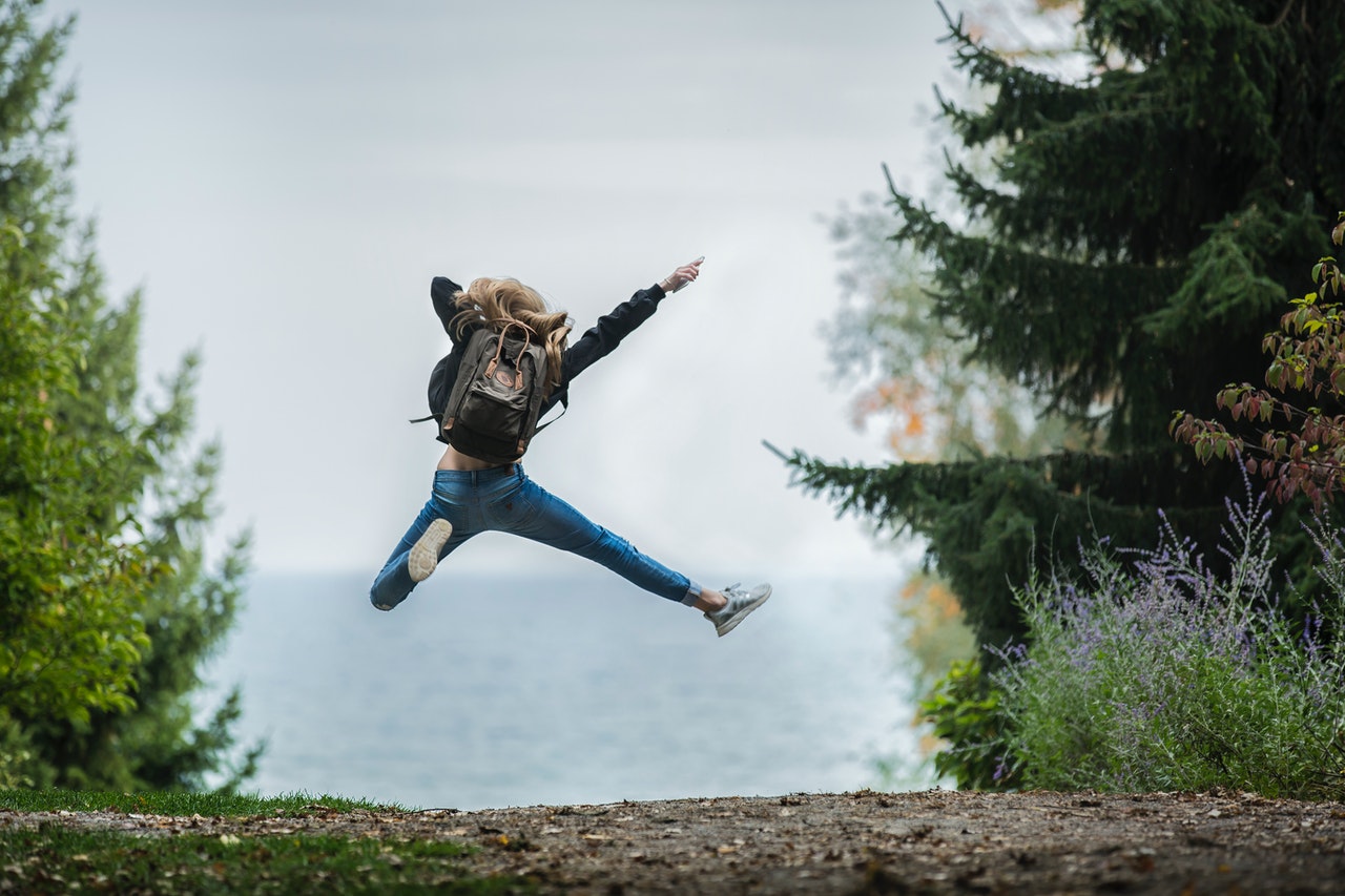 Woman Jumping Freely Wearing Green Backpack